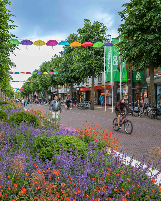 Foto des Stadtzentrums von Uden mit verschiedenen Personen, die mit dem Fahrrad oder zu Fuß unterwegs sind